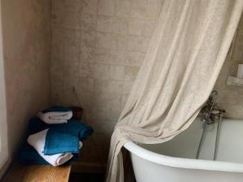 Salle de bain avec baignoire sur pieds derrière un rideau de lin, serviettes pliées sur un banc