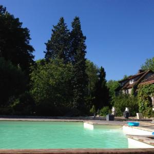 Piscine extérieure bordée de grands arbres, la maison à l'arrière-plan sous un ciel bleu
